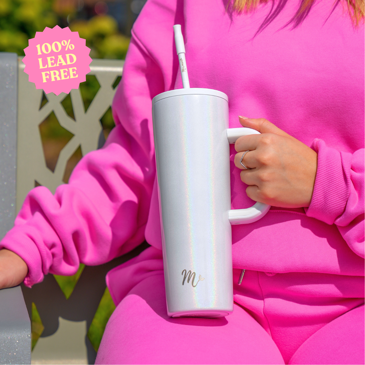 30 oz Pearl Tumbler with Handle and Straw - Lead-Free. Featuring a stylish iridescent pearl finish, this tumbler is showcased by a woman in a pink outfit, highlighting its large ergonomic handle and reusable straw. Perfect for enjoying drinks on the go, while ensuring safety with a 100% lead-free certification.