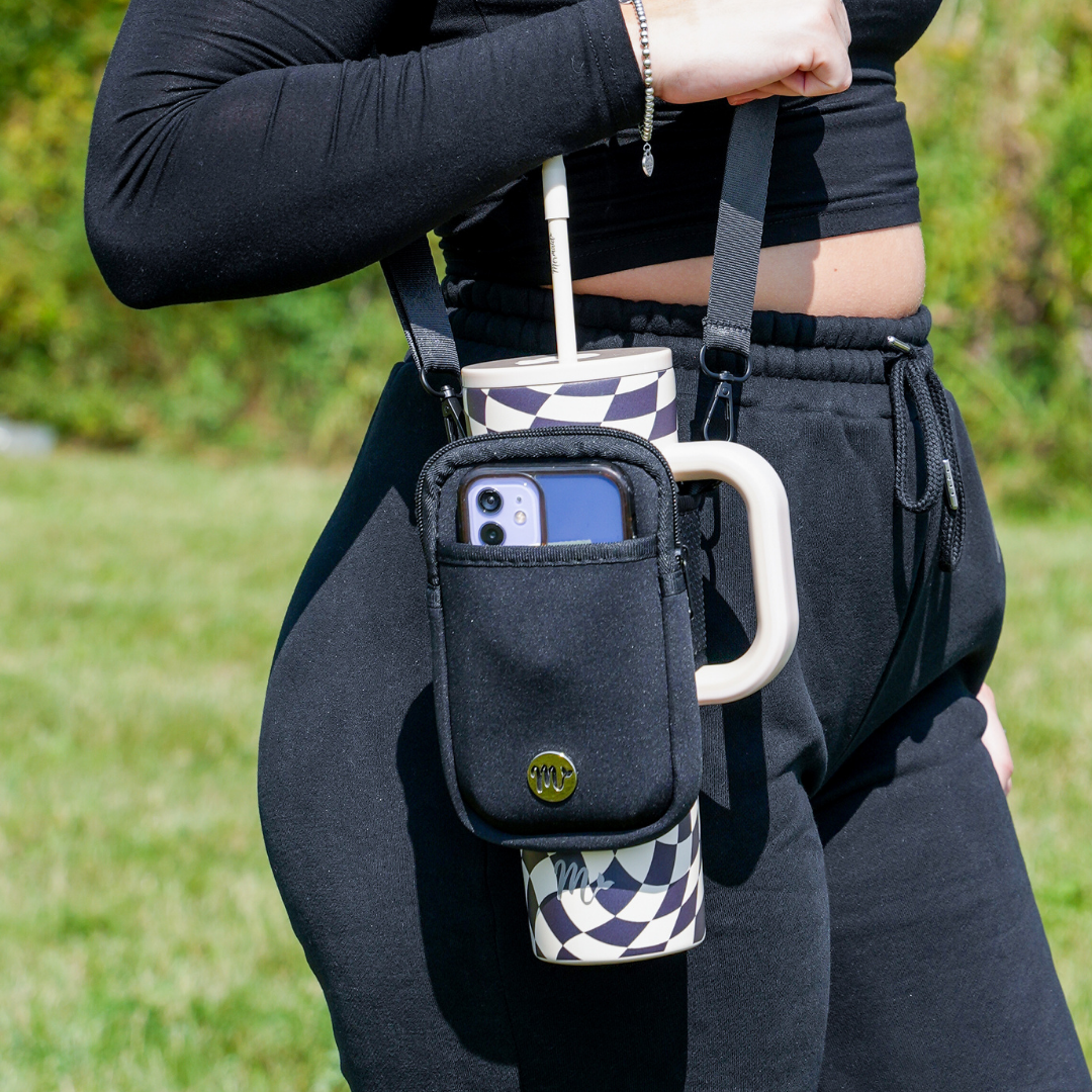 30 oz Checkered Tumbler with Black Sling - A woman carries her checkered tumbler using a black sling pouch, which holds a phone securely in the front pocket. The adjustable strap allows for comfortable, hands-free carrying, making it a practical and stylish accessory for on-the-go activities