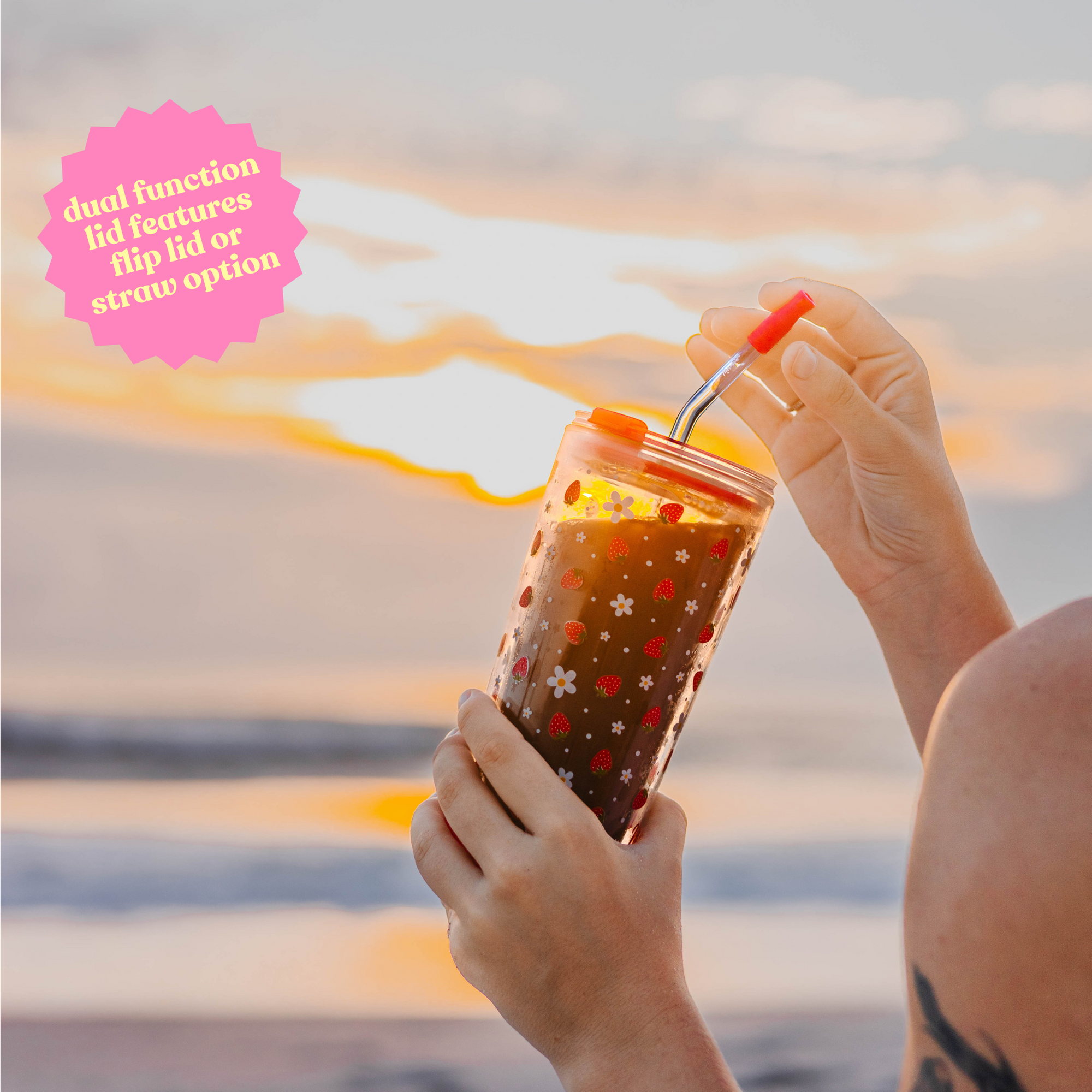 Hands holding a 20oz strawberry-designed double-wall glass cup with text: 'Dual function lid features flip lid or straw option.